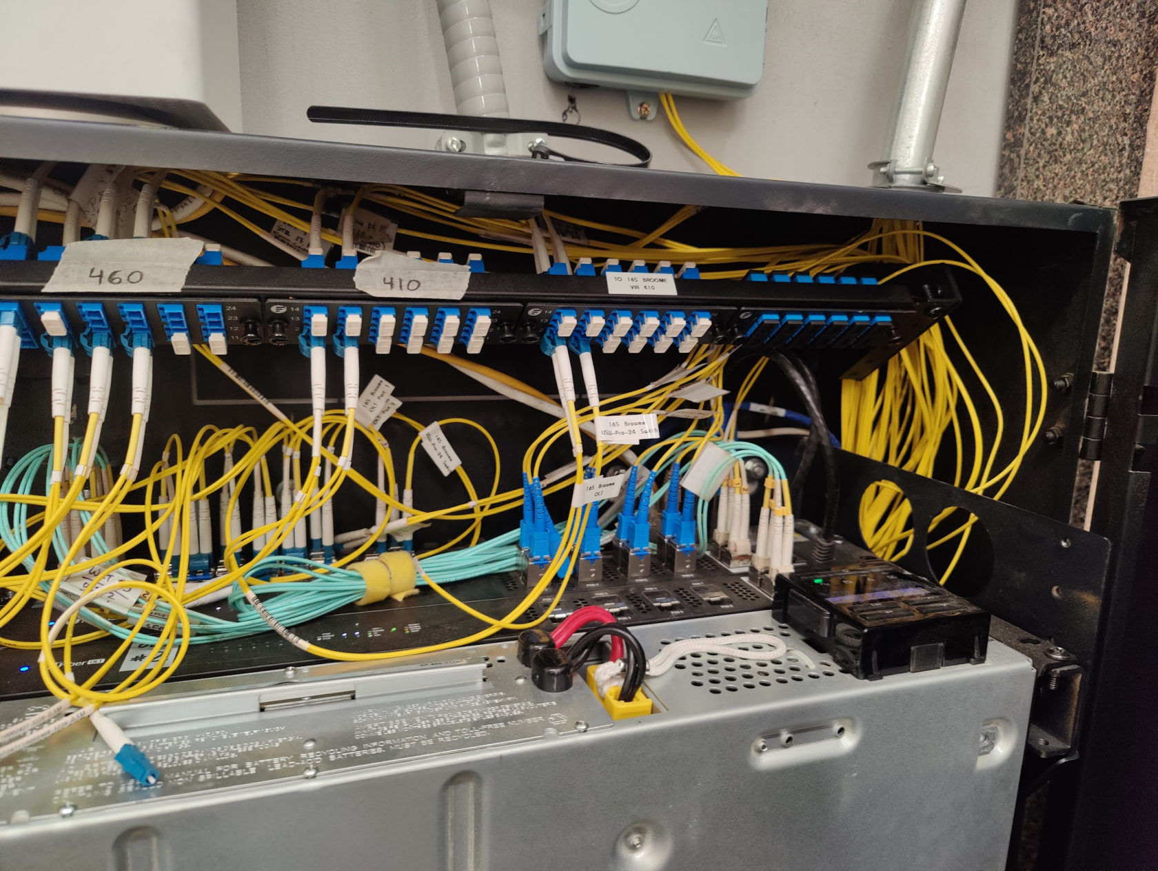 Photo of the inside of a rack at Grand Street Guild. Many yellow fibers are plugged into equipment in the rack
